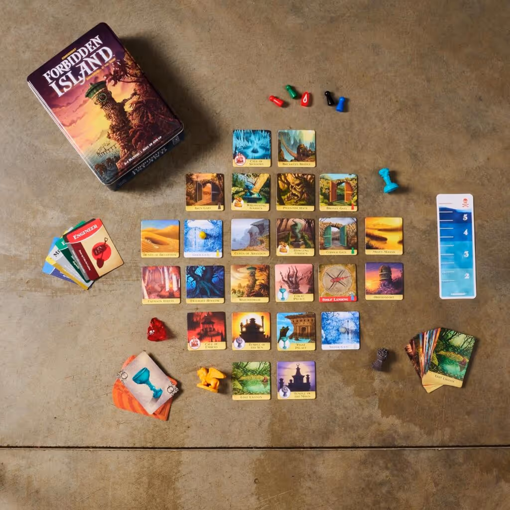Forbidden Island board game components spread out on a table, including the game box, cards, player pawns, and tiles
