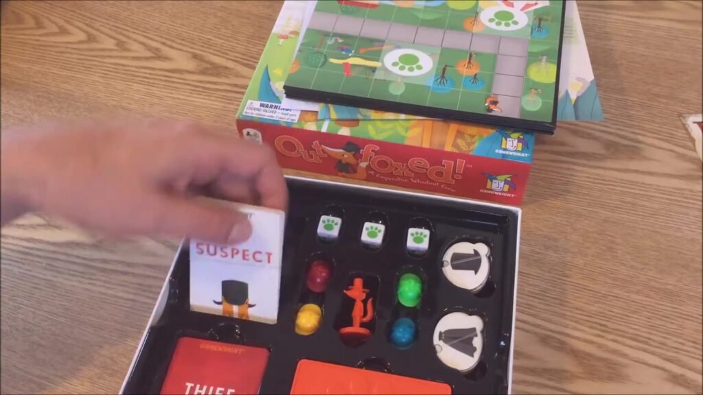 Outfoxed game box and components displayed showing the game board, decoder, suspects, and detective pieces