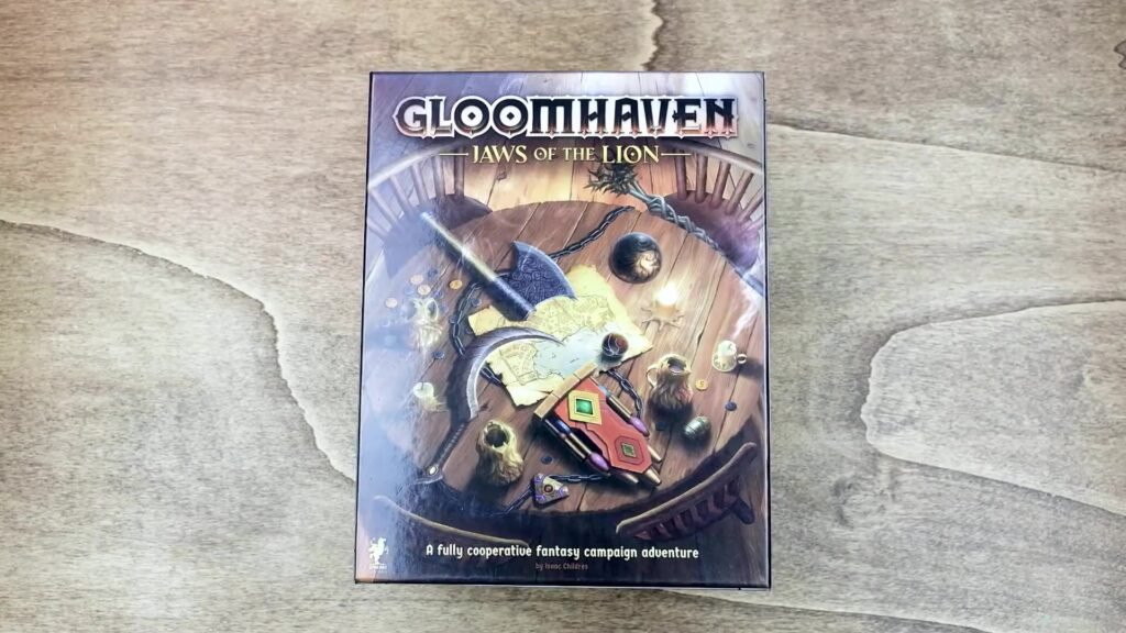 A photograph of the Gloomhaven: Jaws of the Lion board game box, showcasing a detailed illustration of a dungeon scene with characters and a map