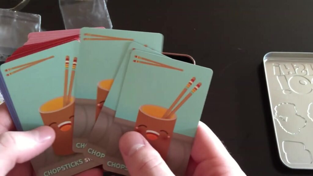 Hands holding Sushi Go! cards featuring chopsticks and a smiling cup