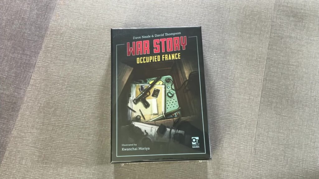 Box of the board game "War Story: Occupied France" on a textured surface, featuring a cluttered desk with wartime items.