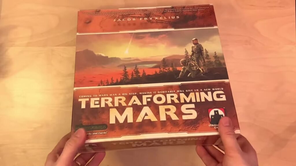 Box of the board game "Terraforming Mars" held by hands, featuring a Martian landscape with astronauts.